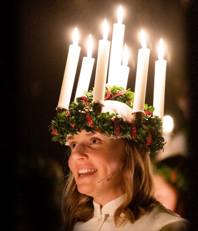 Eine Singende Frau in weißem Kleid trägt eine Kranz mit leuchtenden Kerzen, Foto: rechtefrei