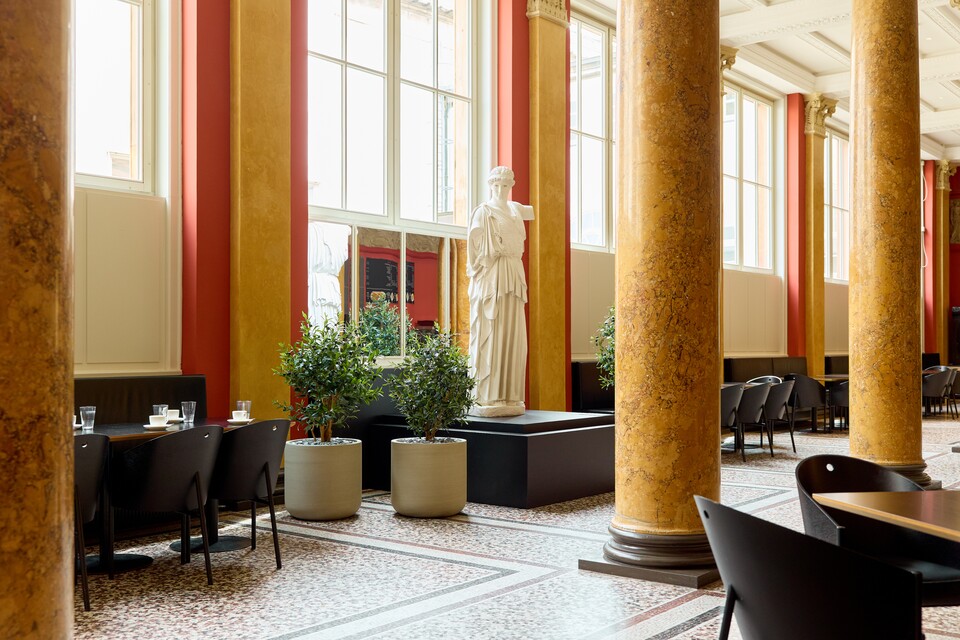 Café mit hohen Säulen, Ledersesseln und natürlichem Licht durch große Fenster