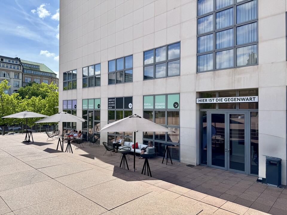 Modernes Gebäude an sonnigem Tag mit Schirmen und Sitzgelegenheiten