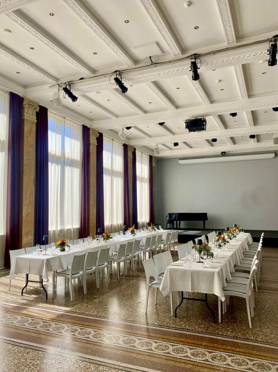 Eleganter Veranstaltungssaal mit weißen Stühlen und hohen Fenstern