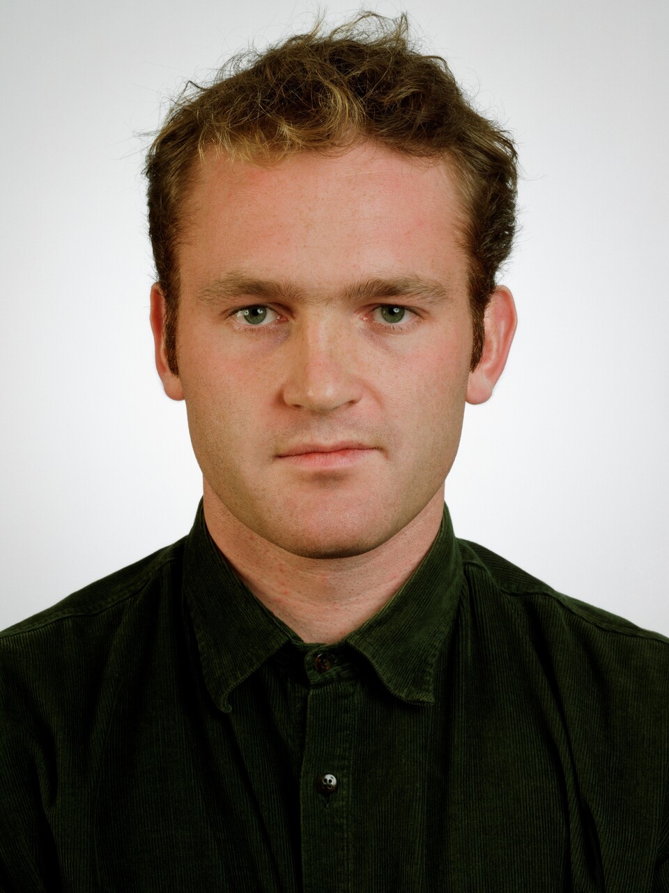 Portraitfoto eines jungen Mannes mit braunem Haar in schwarzem Poloshirt vor weißem Hintergrund