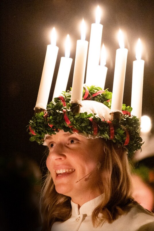 Eine singende Frau in weißem Kleid trägt einen Kranz mit leuchtenden Kerzen, Foto: rechtefrei