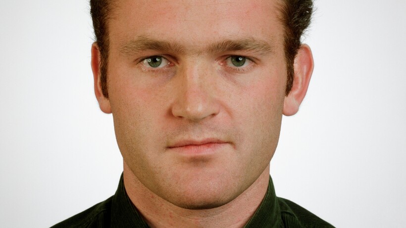Portraitfoto eines jungen Mannes mit braunem Haar in schwarzem Poloshirt vor weißem Hintergrund