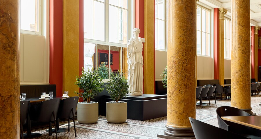 Café mit hohen Säulen, Ledersesseln und natürlichem Licht durch große Fenster
