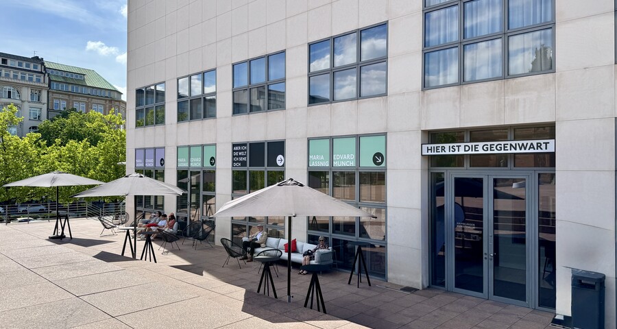 Modernes Gebäude an sonnigem Tag mit Schirmen und Sitzgelegenheiten