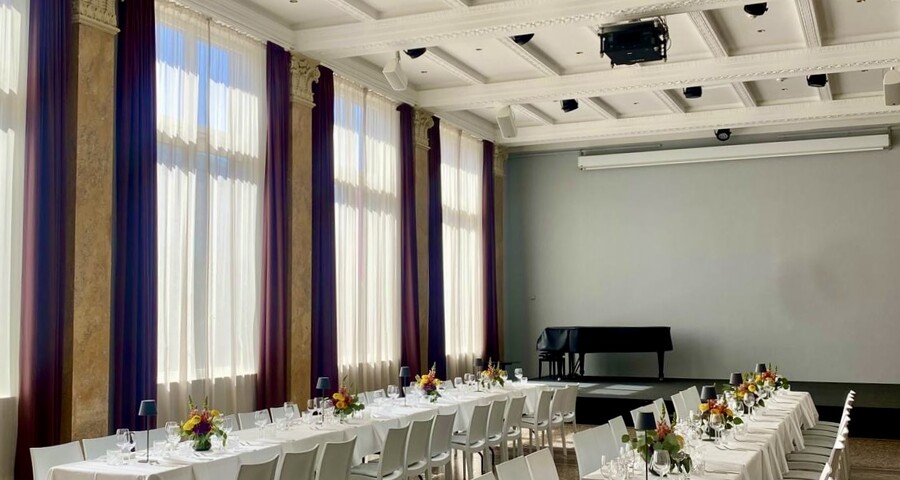 Eleganter Veranstaltungssaal mit weißen Stühlen und hohen Fenstern