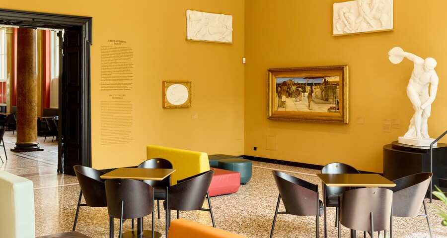 Café mit gelben Wänden, schwarzen Bistrotischen, Stühlen und einer weißen Skulptur